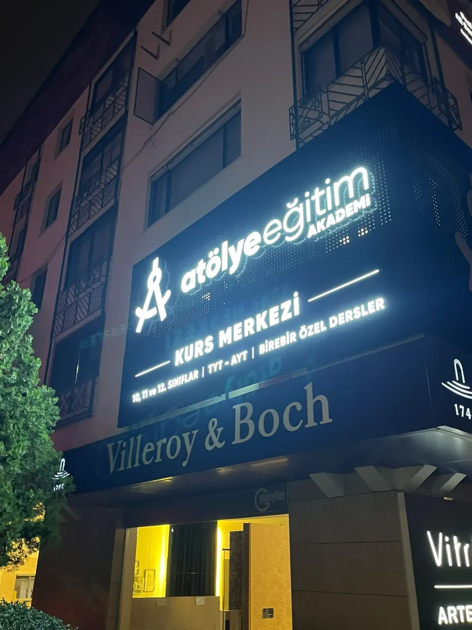 Atölye Eğitim Akademi perfore siyah zemin üzerinde ışıklı kutu harfler, gece açılı çekim